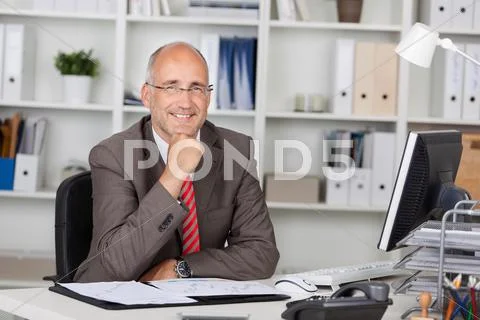 Businessman with hand on chin sitting at desk Stock Photos