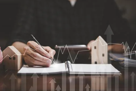 Businessman hand write in book note and icon business graphs with mini wood h Stock Photos
