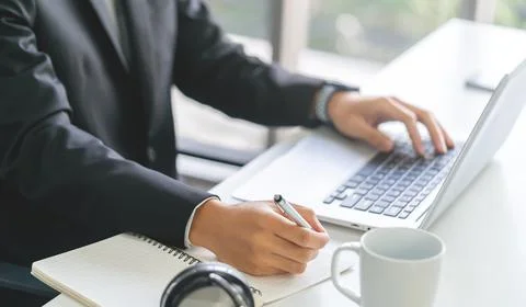 Businessman hand is writing at typing on notebook at the sametime. Stock Photos