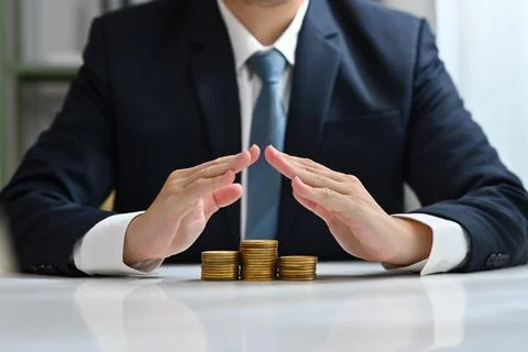 Businessman hands protecting over a stack of coins. Risk, economic recession Stock Photos
