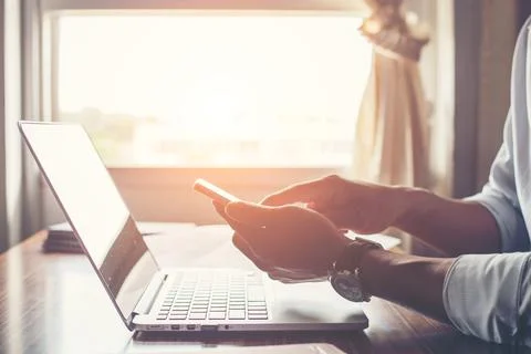 Businessman hands using cell phone with laptop at office desk. Stock Photos