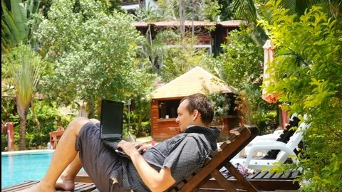 Businessman on his vacation lying on sunbed works on a laptop by swimming pool Stock Footage 88239853