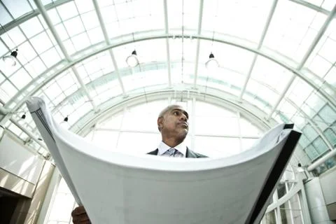 A businessman holding a large plan or architectural drawings standing under a Stock Photos