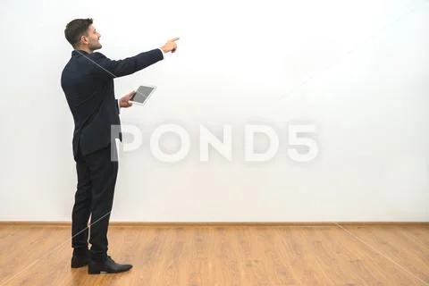 The businessman holding a tablet and gesturing on the white wall background Stock Photos