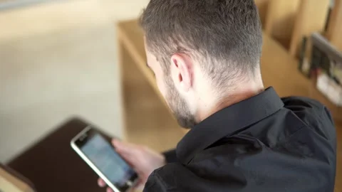Businessman interact with smartphone viewing at screen while seated indoors a Stock Footage 335602658