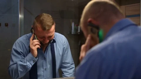 Businessman laughs while chatting with someone on cellphone in the bathroom Stock Footage 73791913