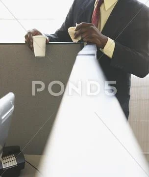 Businessman leaning on cubicle wall while eating Stock Photos