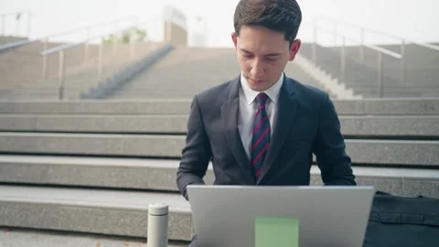 Businessman look at cellphone while using laptop computer sitting on the stairs Stock Footage 272624761