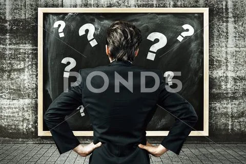 Businessman looking at a billboard with chalk drawn question marks Stock Photos
