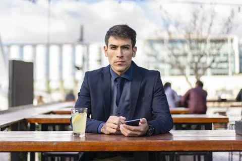 Businessman looking at camera e while holding his smartphone Stock Photos