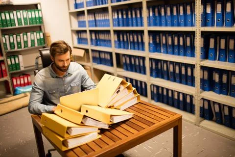 Businessman looking at stack of files on table in storage room Foto stock