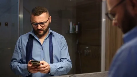 Businessman looks angry while speaking on cellphone with someone in the bathroom Stock Footage 73791853
