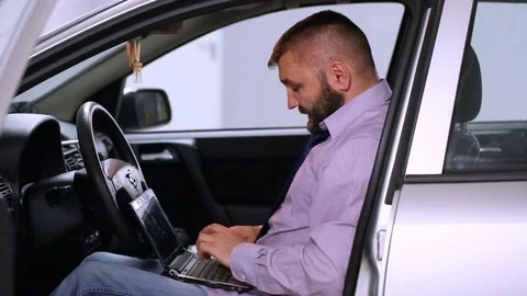 Businessman looks worried while working on laptop inside his car Stock Footage 80396655