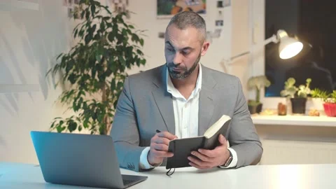 Businessman making notes and holding copybook looking at laptop in office Stock Footage 148556610