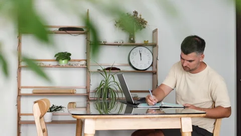 Businessman multitasking writing in a journal and working on his laptop. Stock Footage 310249128