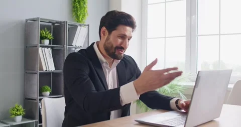 Businessman at office desk talking using laptop engaged in virtual meeting Stock Footage 348573813