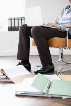 Businessman in office using laptop, documents in foreground, low section Stock Photos