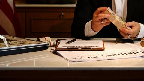 Businessman packing money into briefcase while sitting at office desk Stock Footage