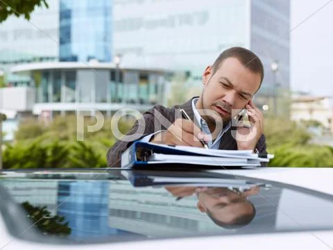 Businessman With Paperwork On Top Of Car