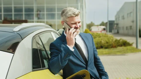 Businessman phoning while charging car at electric vehicle charging station 스톡 동영상 235223320