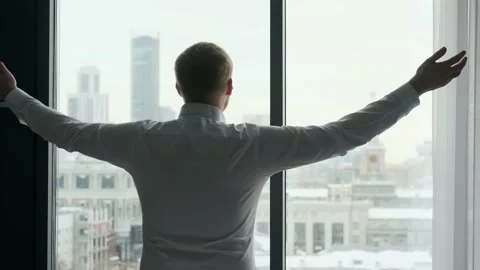 Businessman raises his hands up while standing by the window Stock Footage 135416100
