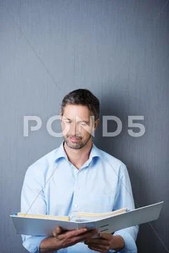 Businessman reading in binder against blue wall Stock Photos