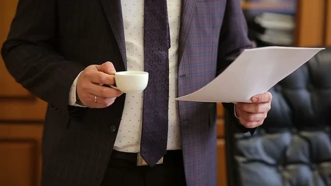 Businessman reading documents and drinks coffee from coffee cup in office Stock Footage 102368668