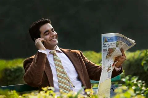 Businessman reading a newspaper while talking on a mobile phone Stock Photos