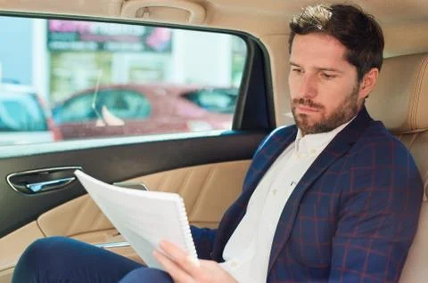 Businessman reading paperwork while being driven through the city Stock Photos