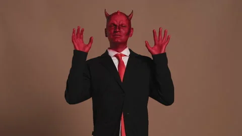 Businessman with red devil makeup meditating on brown background Stock Footage 296240644