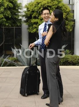 A businessman with a rolling suitcase and a businesswoman sharing a laugh Stock Photos