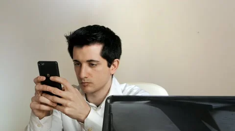 Businessman sends message on his cell phone in front of the PC Stock Footage 61500847