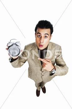 Businessman showing an alarm clock and looking surprised Stock Photos