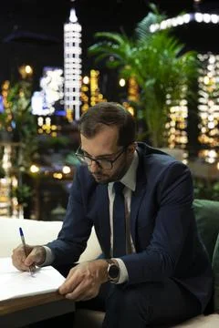 Businessman signing work document while seated at night Foto stock