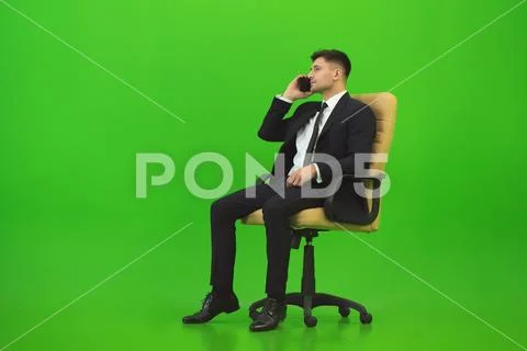 The businessman sit of the chair and call on the green background Stock Photos