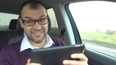 Businessman sits in the car, looking at the tablet screen at good results. Ha Stock Footage 82014010