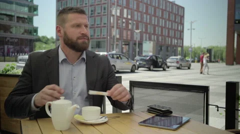Businessman sits down at the table and pours tea into cup, steadicam.. 库存影片 66319101