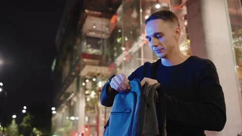 Businessman sits, opens backpack, takes out laptop.Shiny blue light, night scene Stock Footage 275511088