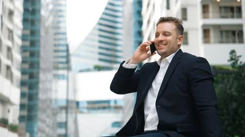 Businessman sitting at bench while talking to manager by using phone. Urbane. 写真素材