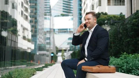 Businessman sitting at bench while talking to manager by using phone. Urbane. 写真素材