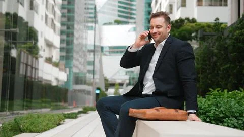 Businessman sitting at bench while talking to manager by using phone. Urbane. Foto stock