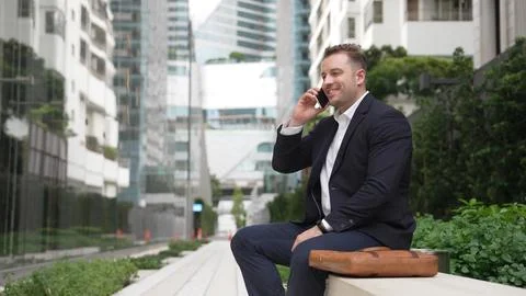 Businessman sitting at bench while talking to manager by using phone. Urbane. 写真素材