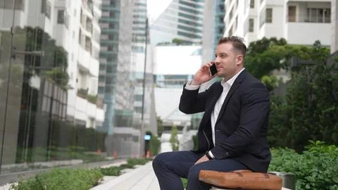 Businessman sitting at bench while talking to manager by using phone. Urbane. Stock Photos
