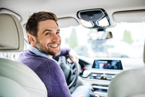 Businessman sitting in brand new car, looking back when driving. Stock Photos