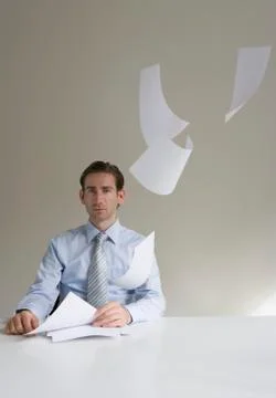 Businessman sitting at desk with paper floating in mid-air Stock Photos