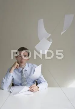 Businessman sitting at desk with paper floating in mid-air Stock Photos