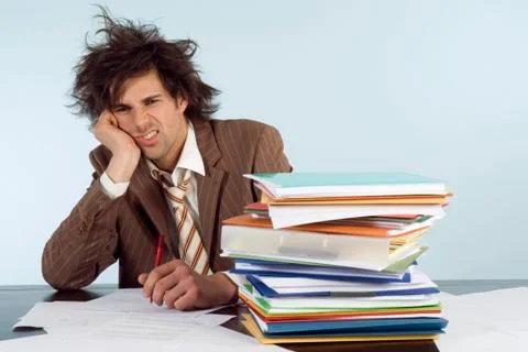 Businessman sitting on desk with stack of file, head in hands, portrait Stockfoto's