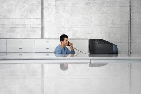 Businessman Sitting In Front Of Computer Using Telephone Stockfoto's