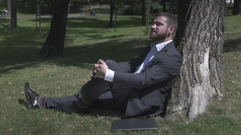Businessman is sitting on ground under tree and relaxing. 库存影片 52770170
