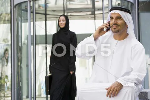 Businessman sitting outdoors by building using cellular phone with businesswoman Stock Photos